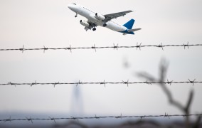 Passenger plane flying behind barbed wire. Macondofotografcisi/Shutterstock. 