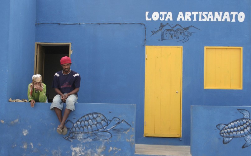 Two people in front of a blue building with yellow doors.